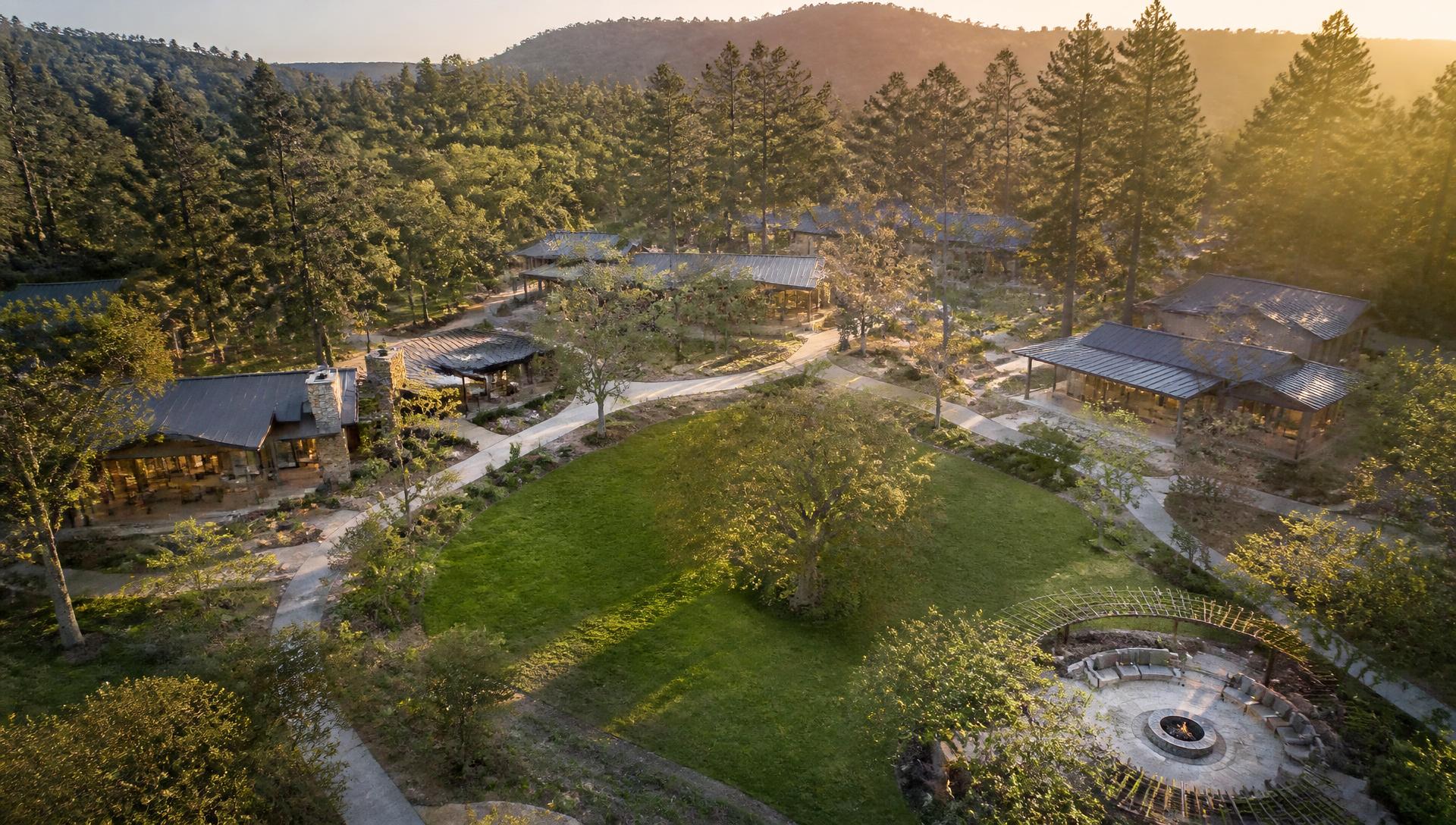 Wellness community concept with cabins, walking paths and an open gathering meadow at golden hour